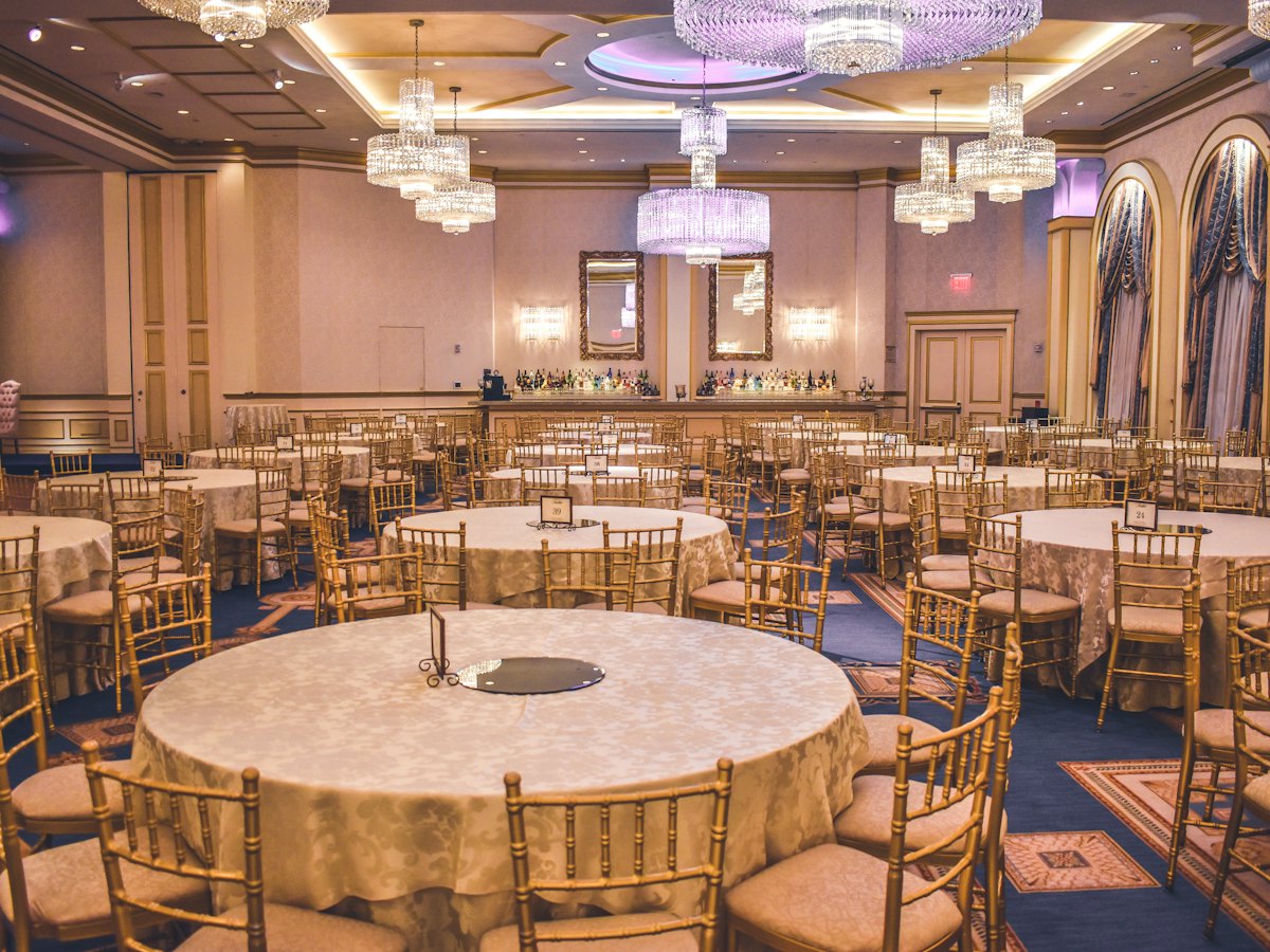 A ballroom with round tables, gold chairs and chandeliers